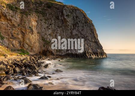 Les vagues tapent doucement contre la rive rocheuse de Crystal Cove Beach, révélant de superbes falaises sous un ciel doré à Laguna Beach, en Californie. Banque D'Images