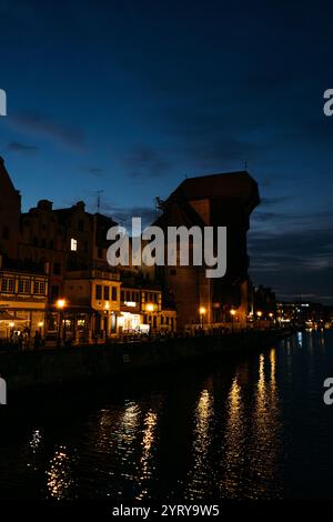 Vue nocturne de la grue historique de Gdansk avec des reflets sur la rivière Motlawa. Monument emblématique polonais illuminé contre un ciel sombre. Gdansk, Pologne - Banque D'Images