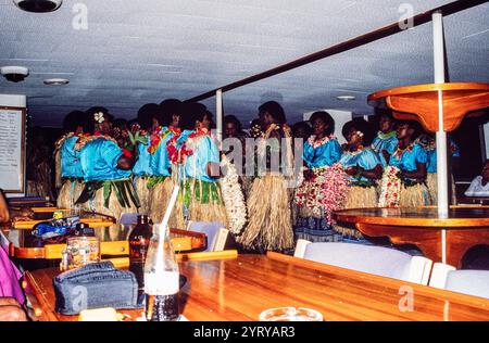 À bord du bateau de croisière Blue Lagoon Cruises aux Fidji, photo d'archives de 1991. Les villageois fidjiens locaux portant des jupes en herbe divertissant les invités à bord du bateau dans la soirée avec un Meke, ou spectacle de danse traditionnelle. Banque D'Images