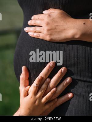 ventre de femme enceinte en robe noire gros plan avec maman et papa et les mains de la fille sur le ventre de maman. Photo de haute qualité Banque D'Images