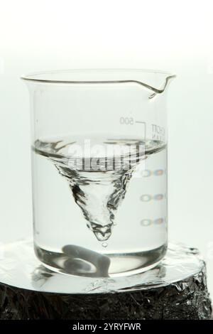 Liquide clair tourbillonnant dans un bécher en verre, créant un vortex lors d'une expérience de laboratoire Banque D'Images