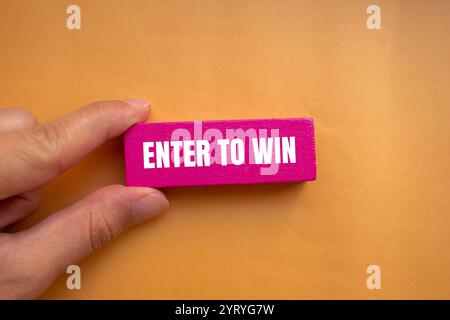 Participez pour gagner un message écrit sur un bloc de bois rose avec un fond orange. Entrez conceptuel pour gagner le symbole. Copier l'espace. Banque D'Images