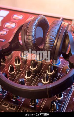 Casque reposant sur une console de mixage DJ dans un éclairage de scène chaleureux, symbolisant la production musicale, la performance DJ et la culture de la vie nocturne. Banque D'Images