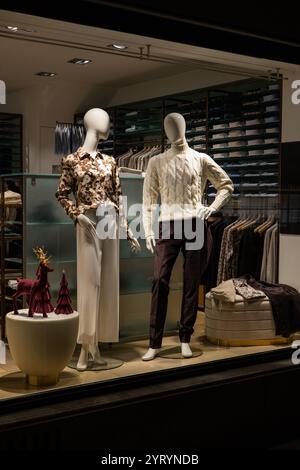 Mannequins féminins et masculins dans l'affichage de la fenêtre en verre de magasin habillés dans l'automne décontracté - vêtements élégants d'hiver, scène de nuit Banque D'Images