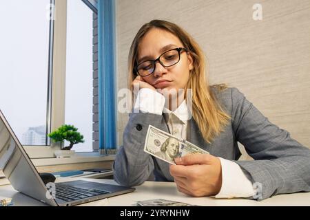 Femme caucasienne comptant de l'argent liquide quantité insuffisante d'argent. Crise financière. Faillite. Pauvreté et misère. Femme d'affaires fille est assise à o Banque D'Images