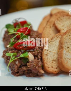 Tartare de bœuf avec poivron rouge et toast sur une assiette blanche Banque D'Images