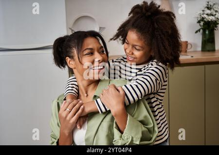 Une mère aimante partage une étreinte joyeuse avec sa fille dans un cadre de cuisine chaleureux. Banque D'Images