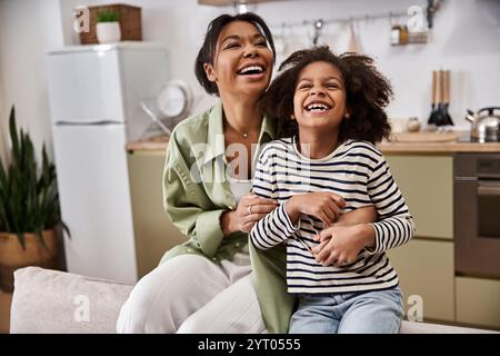 Une mère et sa fille rient ensemble dans une cuisine lumineuse, partageant un moment d'amour. Banque D'Images