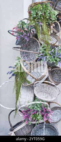 Une collection de paniers en osier disposés verticalement sur un mur, ornés de fleurs artificielles vibrantes, y compris la lavande, les fougères et les fleurs colorées. Banque D'Images