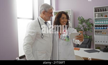 Des médecins souriants prenant un selfie dans une salle de bureau d'hôpital, mettant en valeur le travail d'équipe et le professionnalisme de la santé dans un environnement de travail lumineux. Banque D'Images