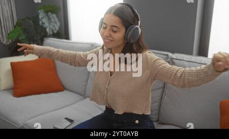 Femme se relaxant avec des écouteurs dans un intérieur confortable de la maison, profiter de la musique sur un canapé avec les yeux fermés, créant une atmosphère sereine dans un salon moderne Banque D'Images