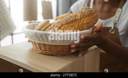 Femme afro-américaine tenant un panier de pain fraîchement cuit dans un intérieur de boulangerie. Banque D'Images