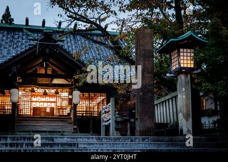 Une vue tranquille sur un sanctuaire japonais, illuminé par des lanternes et entouré de belles feuilles d'automne Banque D'Images