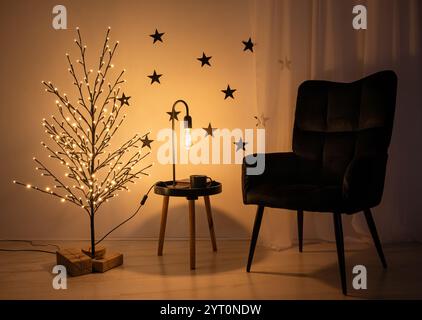Concept alternatif d'arbre de Noël. Arbre minimaliste en fil de couleur noire avec lumières éclairées la nuit. Fauteuil noir, cadeaux sous l'arbre. Banque D'Images