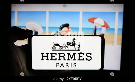 Dans cette illustration photo, une personne tient un smartphone avec le logo de la société de luxe française Hermes International S.A. en face de son site web. Banque D'Images