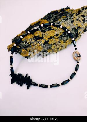 Collier de perles en pierre noire à fond rose gros plan sur l'écorce d'arbre avec arrangement de lichen. Hématite, choker en pierre semi-précieuse magnétite Banque D'Images