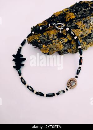 Collier de perles en pierre noire à fond rose gros plan sur l'écorce d'arbre avec arrangement de lichen. Hématite, choker en pierre semi-précieuse magnétite Banque D'Images