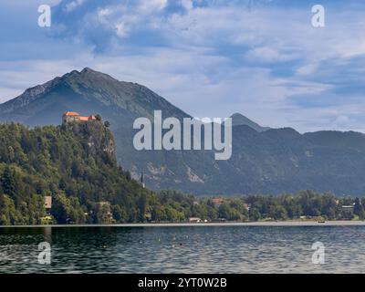 Lac de Bled, Slovénie - 28 juin 2024 : le château médiéval de Bled avec ses toits rouges se dresse au-dessus du lac sur sa roche boisée sous un paysage nuageux bleu. Foreste Banque D'Images