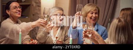 Groupe d'amis animés, des femmes âgées se réunissant à la maison, assis dans un salon chaleureux et éclairé, parlant et buvant du vin Banque D'Images