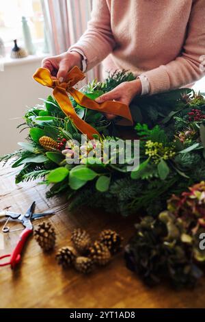 Gros plan de la femme faisant et décorant couronne de Noël festive sur la table à la maison attache Bow fait de ruban Banque D'Images