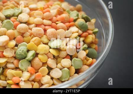 Diverses légumineuses fendues colorées dans un bol en verre sur un fond noir. (pois, lentilles). Gros plan. Banque D'Images