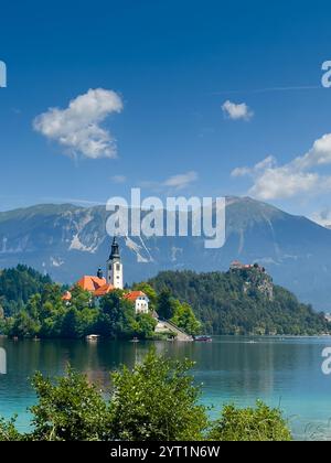 Lac de Bled, Slovénie - 28 juin 2024 : église de l'Assomption de la Bienheureuse Vierge Marie sur la petite île avec les toits rouges et la tour et le château Banque D'Images