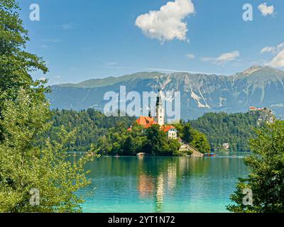Lac de Bled, Slovénie - 28 juin 2024 : église de l'Assomption de la Bienheureuse Vierge Marie sur la petite île avec les toits rouges et la tour et le château Banque D'Images