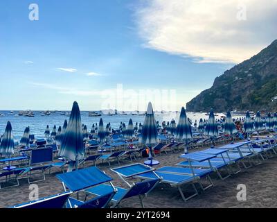 Positano, Italie - 5 août 2022 : plage pittoresque de Positano avec parasols bleus, chaises longues, mer scintillante, falaises et bateaux dans une plage méditerranéenne Banque D'Images