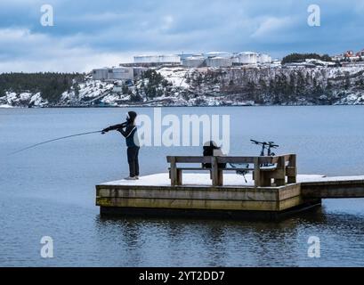 Stockholm, Suède - 26 février 2023 : un pêcheur seul attrape du poisson dans la mer Baltique au milieu de l'hiver, debout sur une jetée en bois où il roulait Banque D'Images