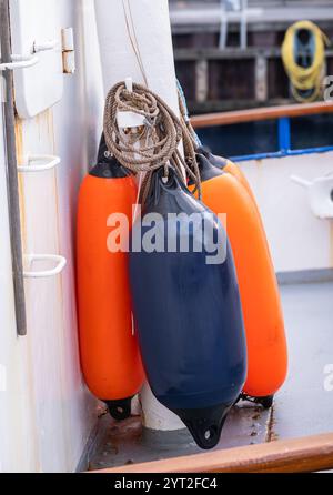 Gros plan des défenses d'un bateau, présentant des bouées orange et bleues durables fixées à un poteau. Banque D'Images