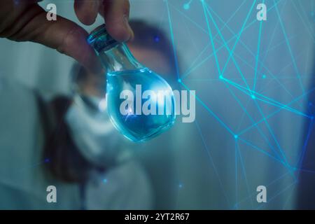 Un scientifique portant des lunettes de protection tient une fiole à fond rond avec un liquide bleu brillant dans un laboratoire. Expérience de chimie, recherche et scient Banque D'Images