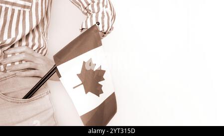 Étudiante non reconnue en chemise bleue blanche tenant un petit drapeau canadien sur fond gris, fête du Canada, mousse Mocha couleur de l'année. Banque D'Images