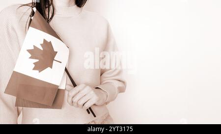 Étudiante non reconnue en chemise bleue blanche tenant un petit drapeau canadien sur fond gris, fête du Canada, mousse Mocha couleur de l'année. Banque D'Images