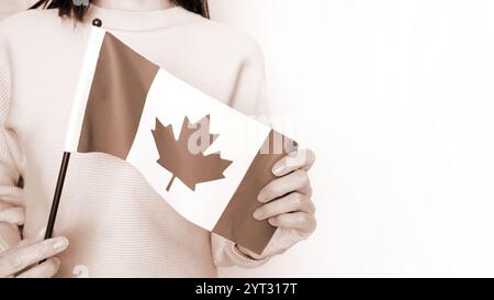 Étudiante non reconnue en chemise bleue blanche tenant un petit drapeau canadien sur fond gris, fête du Canada, mousse Mocha couleur de l'année. Banque D'Images