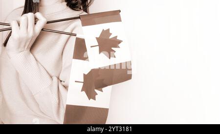 Étudiante non reconnue en chemise bleue blanche tenant un petit drapeau canadien sur fond gris, fête du Canada, mousse Mocha couleur de l'année. Banque D'Images