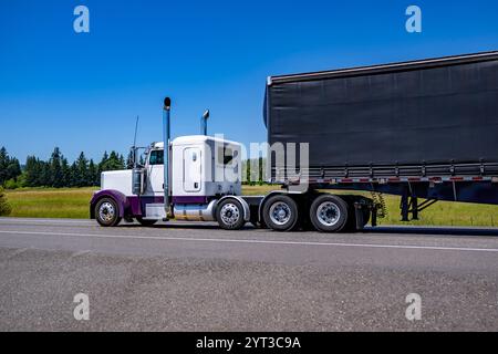 Industriel blanc et violet Big Rig semi-camion classique avec cabine prolongée pour le repos de conducteur de camion transportant des marchandises en noir conestoga plat mauvais semi tra Banque D'Images