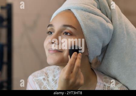 Belle jeune fille avec des yeux noisette, des lèvres rose vif et utilise une éponge humide faciale naturelle. Routine de beauté biologique pour le massage, nettoyage profond des pores a Banque D'Images