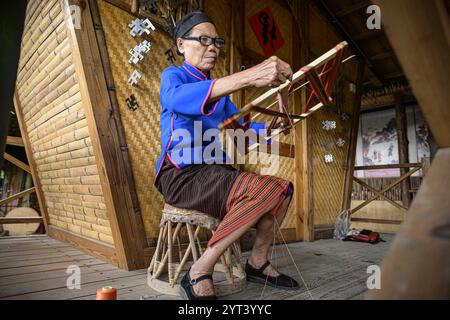 (241206) -- PÉKIN, 6 décembre 2024 (Xinhua) -- une femme âgée du groupe ethnique Li démontre les techniques de filage de la fabrication de brocart Li dans la zone touristique de Binglanggu dans le comté autonome de Baoting Li et Miao, dans la province de Hainan du sud de la Chine, 4 novembre 2024. Trois éléments culturels chinois, à savoir les techniques textiles traditionnelles Li : filature, teinture, tissage et broderie, fête du nouvel an de Qiang, célébrée dans la province chinoise du Sichuan, et la conception et les pratiques traditionnelles pour la construction de ponts en arc de bois chinois, ont été ajoutés par l'UNESCO à sa liste représentative du patrimoine culturel immatériel de Hum Banque D'Images