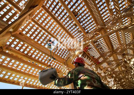 (241206) -- PÉKIN, Dec. 6, 2024 (Xinhua) -- des ouvriers lèvent des tuiles pour restaurer le toit du pont Wan'an, un pont en arc de bois, dans le canton de Changqiao du comté de Pingnan, province du Fujian, au sud-est de la Chine, novembre 29, 2023. Trois éléments culturels chinois, à savoir les techniques textiles traditionnelles Li : filature, teinture, tissage et broderie, fête du nouvel an de Qiang, célébrée dans la province chinoise du Sichuan, et la conception et les pratiques traditionnelles pour la construction de ponts en arc de bois chinois, ont été ajoutés par l'UNESCO à sa liste représentative du patrimoine culturel immatériel de l'humanité lors de la 19e sessi Banque D'Images