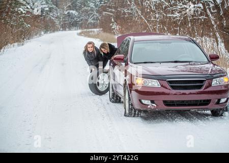 Fille remplaçant les pneus. Voiture de défaut en hiver. Femmes essayant de réparer la voiture, réparation de moteur, changement de pneu. Femelle utilisant la roue de changement. Femmes Banque D'Images
