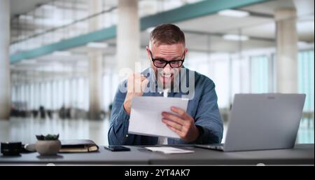 Young Businessman Smiling While Reading Paper At Desk In Office Banque D'Images