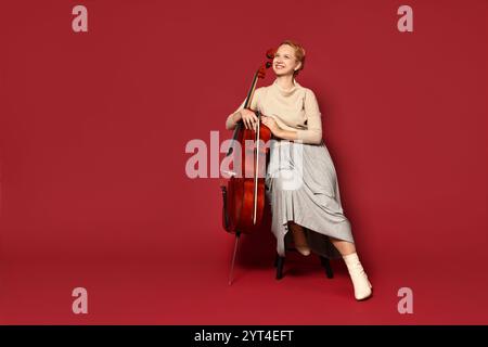 Belle jeune femme avec violoncelle sur fond rouge Banque D'Images