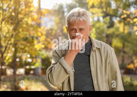 Homme senior avec le nez qui coule dans le parc, espace pour le texte Banque D'Images