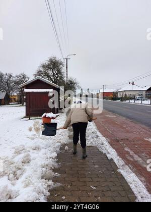 femme villageoise dégageant la neige avec une pelle du sentier du village zala county hongrie Banque D'Images