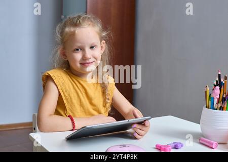 Une petite fille heureuse joue avec une tablette. Utilise le gadget pour l'apprentissage et la communication. Apprécie le contenu vidéo ou photo intéressant sur les réseaux sociaux Banque D'Images