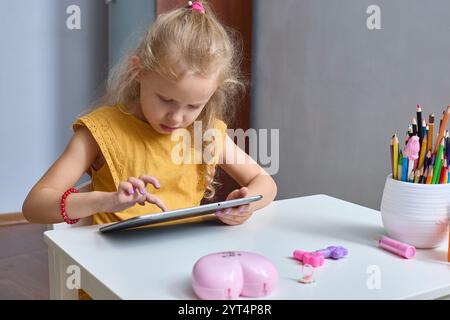 Une petite fille heureuse joue avec une tablette. Utilise le gadget pour l'apprentissage et la communication. Apprécie le contenu vidéo ou photo intéressant sur les réseaux sociaux Banque D'Images