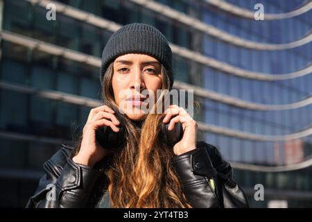 Jeune femme élégante portant des écouteurs en milieu urbain Banque D'Images