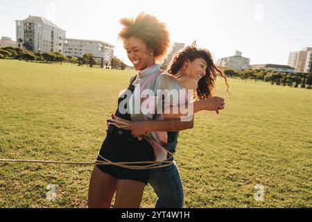 Deux amies riant et jouant à l'extérieur. Ils sont tissés ensemble avec une corde qui symbolise leur lien étroit, profitant d'un moment ludique avec Banque D'Images