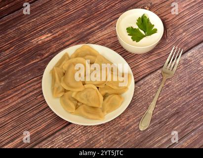 Boulettes fraîchement cuites sur une assiette ronde en céramique sur une table en bois, à côté d'une tasse avec de la crème sure et une fourchette. Vue de dessus, pose à plat. Banque D'Images