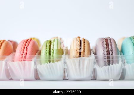 Macarons français avec paperpan blanc dans une boîte d'emballage transparente en plastique sur fond gris, gâteaux colorés avec diverses saveurs. dessert appétissant, Banque D'Images